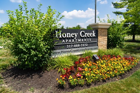 a sign for honey creek apartments in front of a flower garden